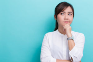 Asian woman thinking in front of blue background.